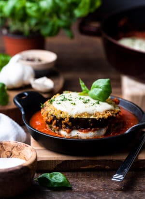 Quinoa crusted eggplant parmesan stacked in a black dish with marinara sauce.