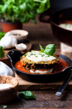 Quinoa crusted eggplant parmesan stacked in a black dish with marinara sauce.