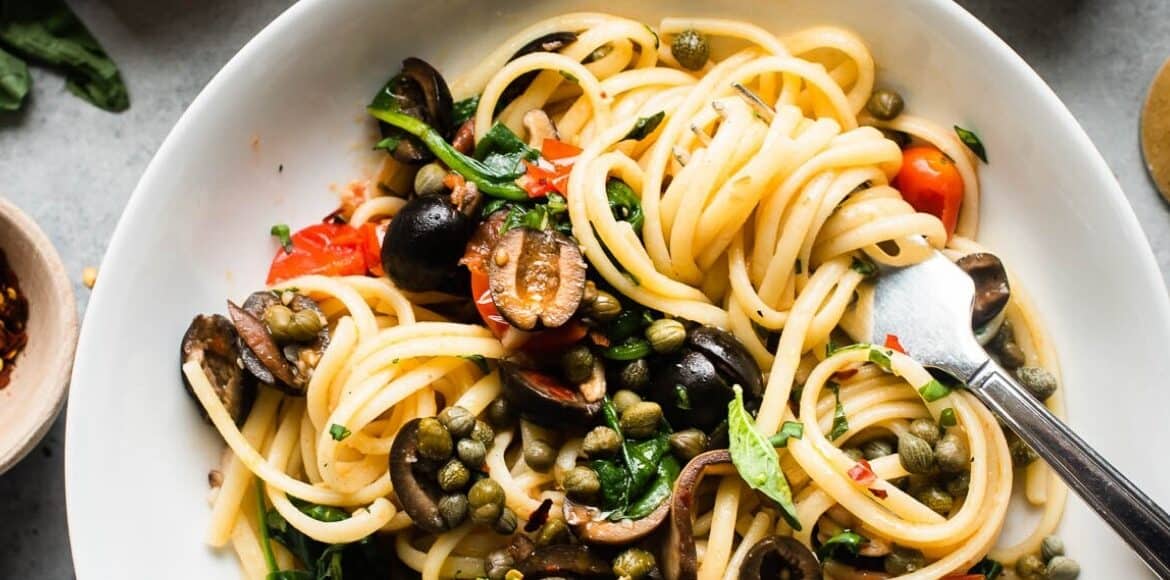 A dish with pasta, olives, and capers.