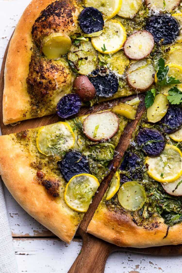 Potato Pesto Pizza with Brussels Sprouts and Yellow Squash sliced on a cutting board.