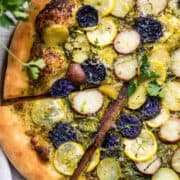 Potato Pesto Pizza with Brussels Sprouts and Yellow Squash sliced on a wood cutting board.