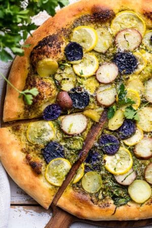 Potato Pesto Pizza with Brussels Sprouts and Yellow Squash sliced on a wood cutting board.