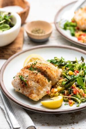 Quinoa Stuffed Sole with spinach and peppers on a white dish with greens on the side.