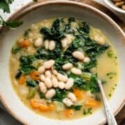 White bean soup with kale, spinach and veggies in a cream-colored bowl and croutons on the side.