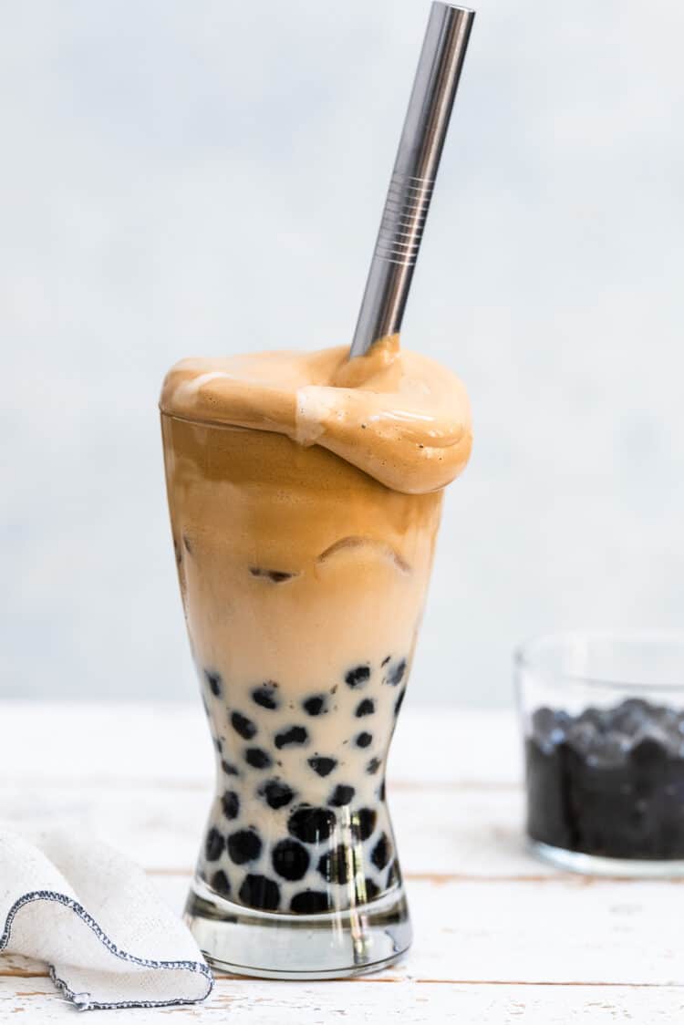 Dalgona Coffee with Boba in a tall glass with tapioca pearls, milk, whipped coffee and a metal straw.