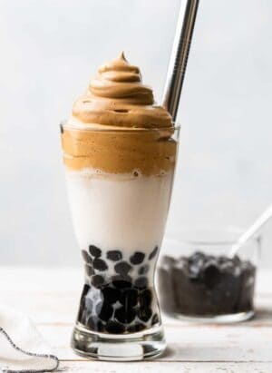 Dalgona Coffee with Boba in a tall glass with tapioca pearls, milk, whipped coffee and a metal straw.
