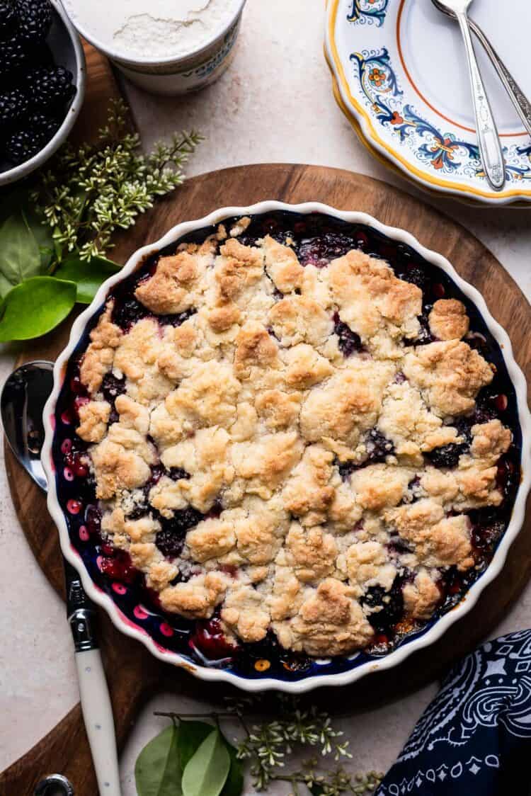 Brombeer-Crumble in einer Keramik-Kuchenform auf einem Holzbrett.