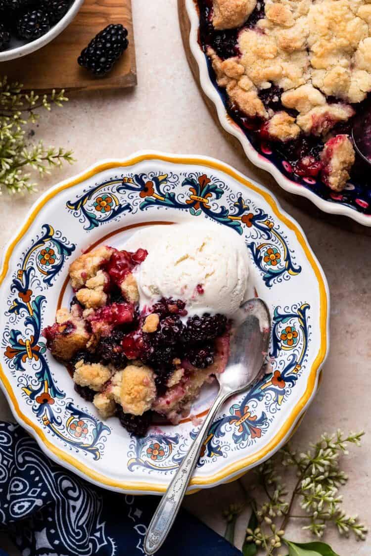 Blackberry Crumble with vanilla ice cream served on a yellow edged plate with a spoon.