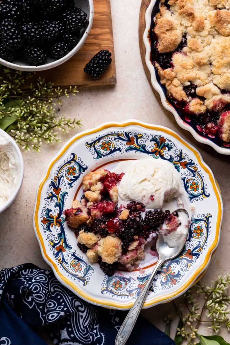 Blackberry Crumble with vanilla ice cream served on a yellow edged plate with a spoon.