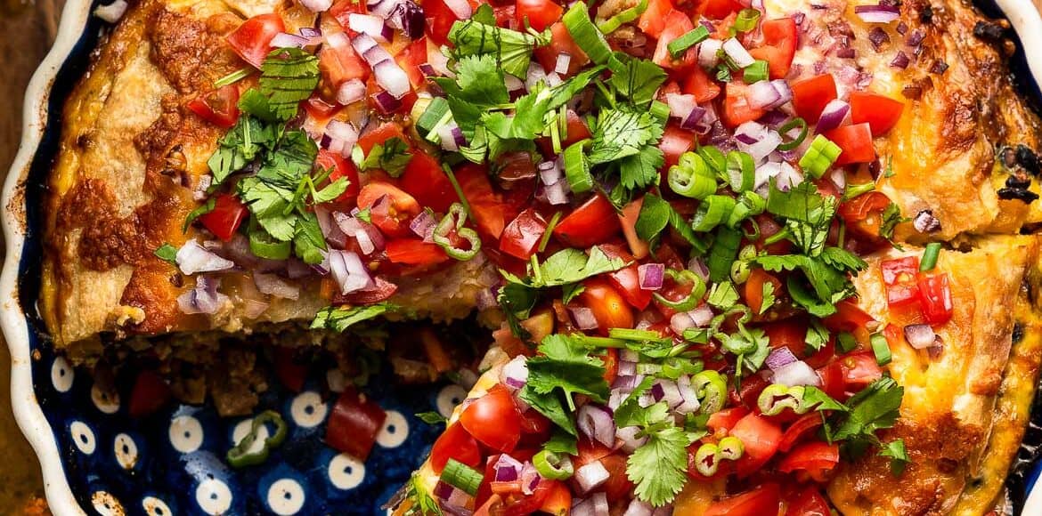 Breakfast Tortilla Pie, a tortilla casserole in a pie dish sliced, topped with onions, tomatoes, green onions and cilantro.