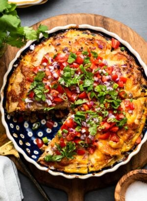 Breakfast Tortilla Pie, a tortilla casserole in a pie dish sliced, topped with onions, tomatoes, green onions and cilantro.