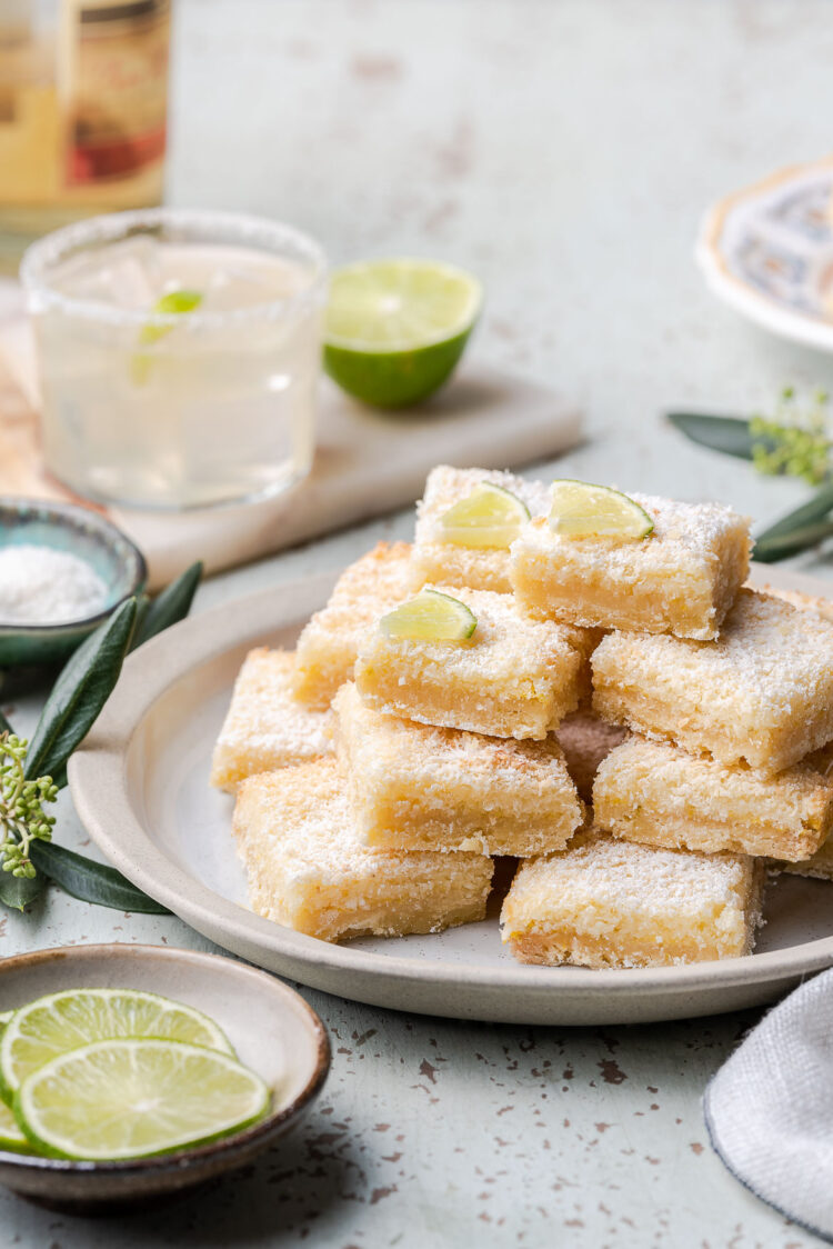 A stack of margarita bars on a white plate with a margarita in the background.