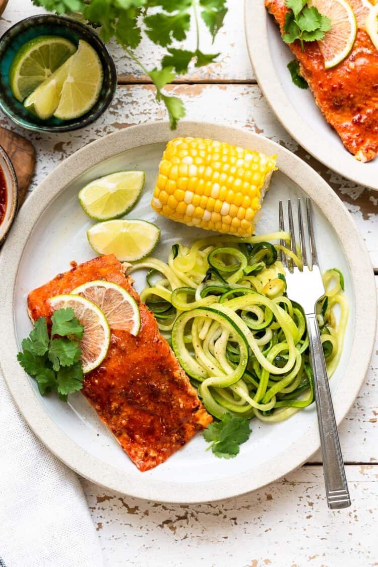 Plank Grilled Salmon with Honey Chipotle Glaze on a plate with zucchini noodles and corn.