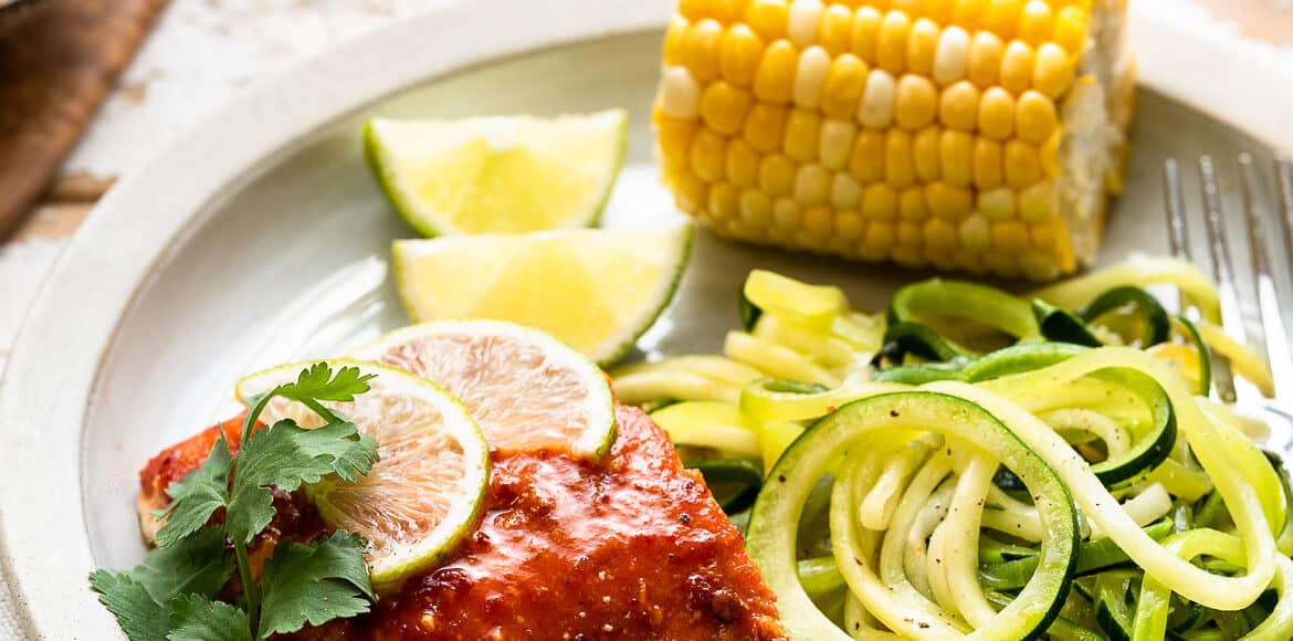 Plank Grilled Salmon with Honey Chipotle Glaze on a plate with zucchini noodles and corn.