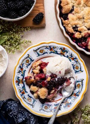 Blackberry Crumble with vanilla ice cream served on a yellow edged plate with a spoon.