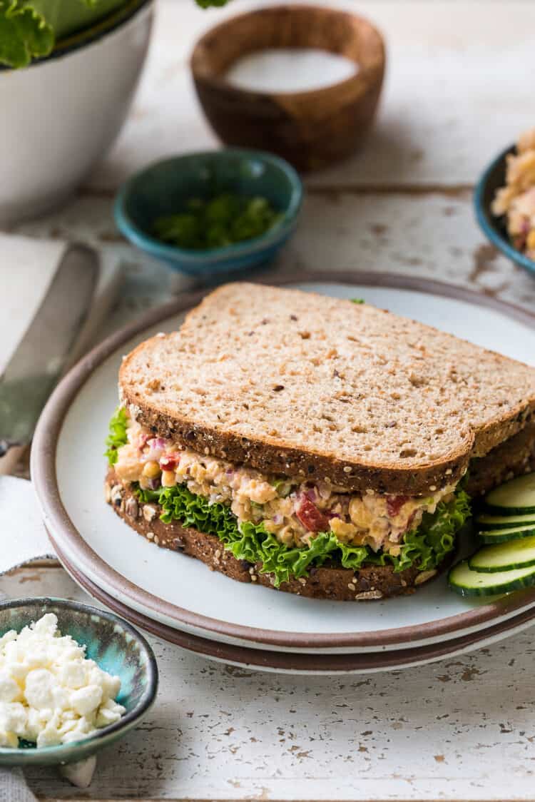 Chickpea Salad Sandwich with Feta on whole wheat bread, with green leaf lettuce on a white plate.