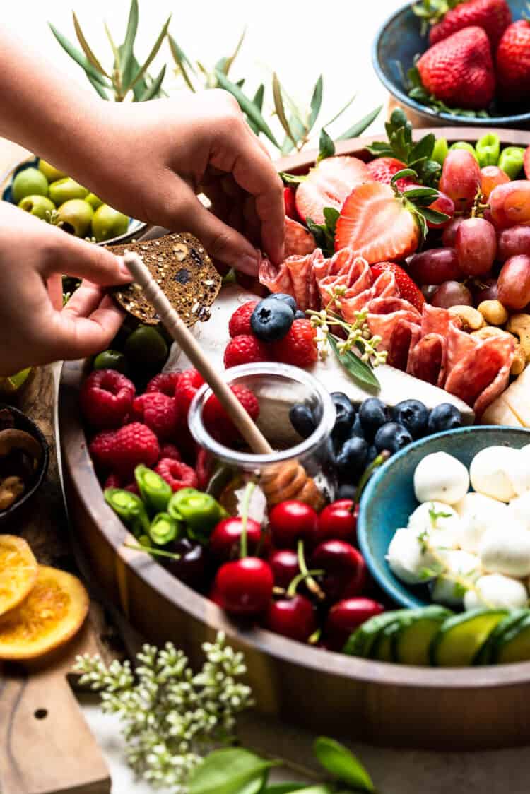 Snacking from a cheese and charcuterie board with fresh fruits and vegetables.