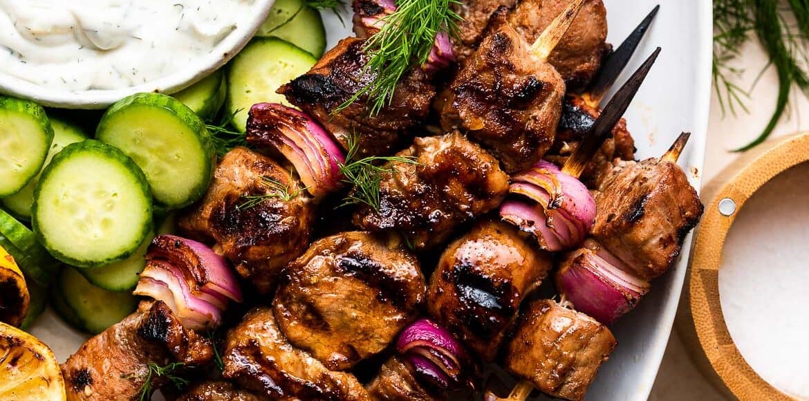 Grilled Pork Skewers made with Balsamic Marinade on a white serving platter with tzatziki and fresh vegetables.
