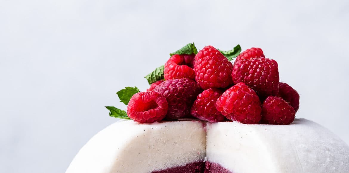 Vanilla Raspberry Ice Cream Bombe topped with fresh raspberries and mint, sliced on a white plate.