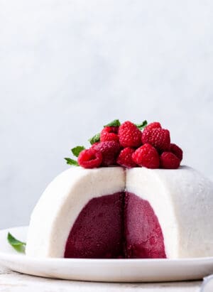 Vanilla Raspberry Ice Cream Bombe topped with fresh raspberries and mint, sliced on a white plate.