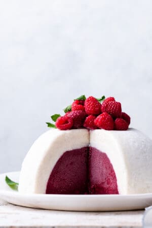 Vanilla Raspberry Ice Cream Bombe topped with fresh raspberries and mint, sliced on a white plate.