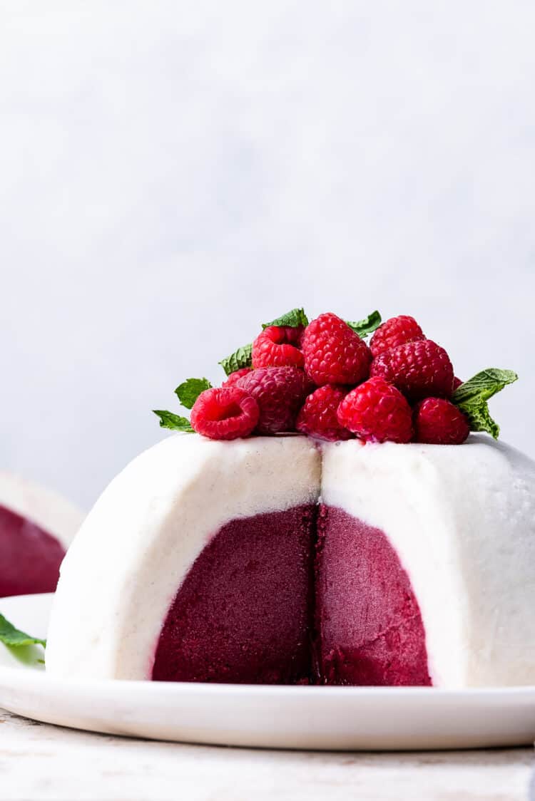 Vanilla Raspberry Ice Cream Bombe topped with fresh raspberries and mint, sliced on a white plate.