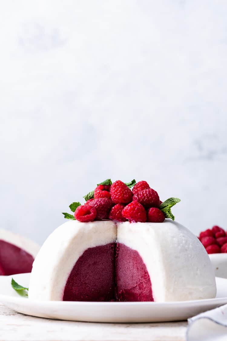 Vanilla Raspberry Ice Cream Bombe topped with fresh raspberries and mint, sliced on a white plate.