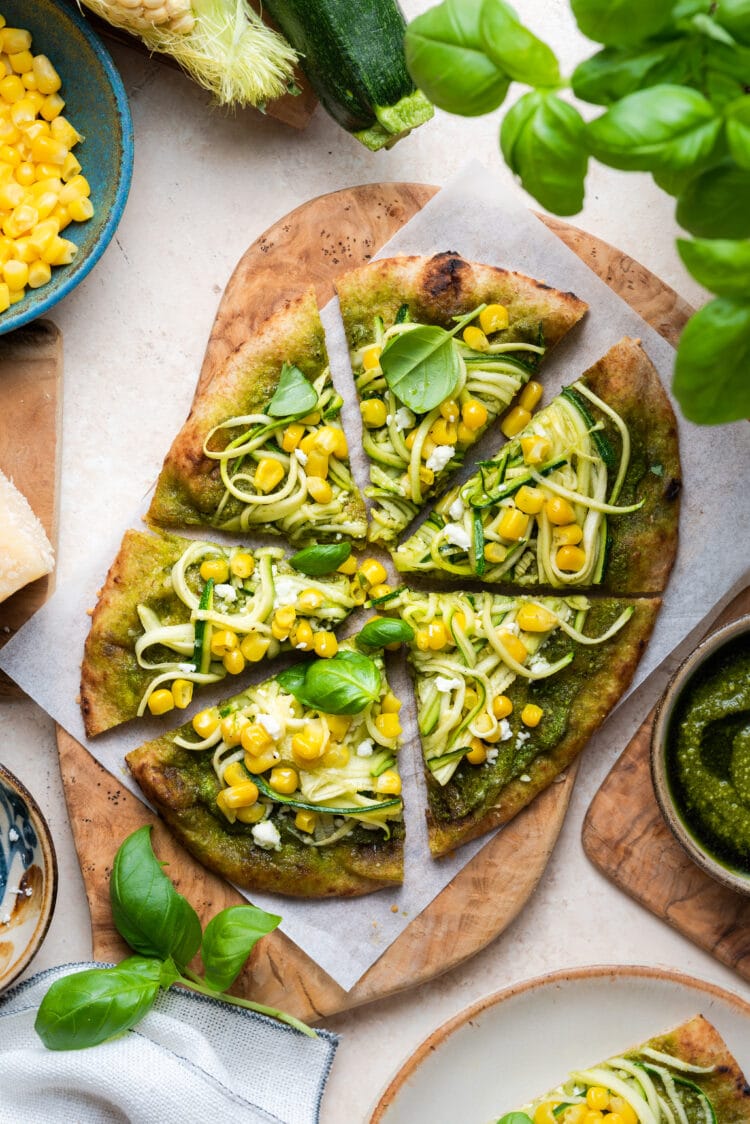 Zucchini, Corn and Pesto Flatbread sliced on a wooden cutting board.