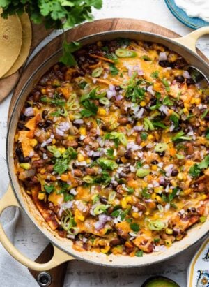 Vegetarian Enchilada casserole in a yellow skillet on a white wooden table.