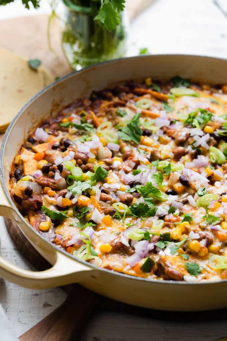 Vegetarian Enchilada casserole in a yellow skillet on a white wooden table.