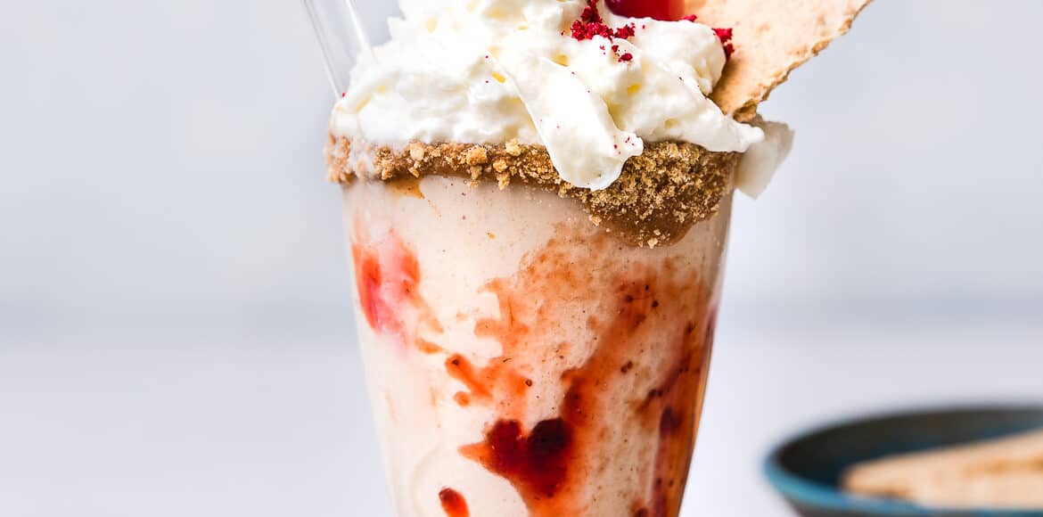 Almond Butter and Jelly Vegan Milkshake in a glass topped with non-dairy whipped cream, graham crackers and a maraschino cherry.