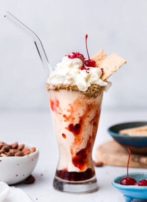 Almond Butter and Jelly Vegan Milkshake in a glass topped with non-dairy whipped cream, graham crackers and a maraschino cherry.