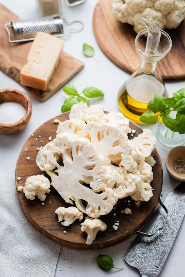 Cauliflower steaks sliced on a cutting board on a grey table.