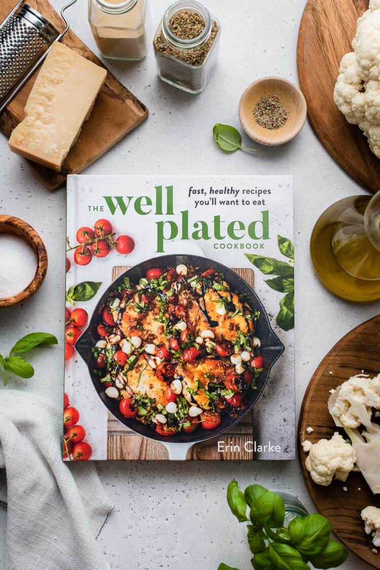 Well Plated Cookbook on a grey table with ingredients for Baked Cauliflower Parmesan.