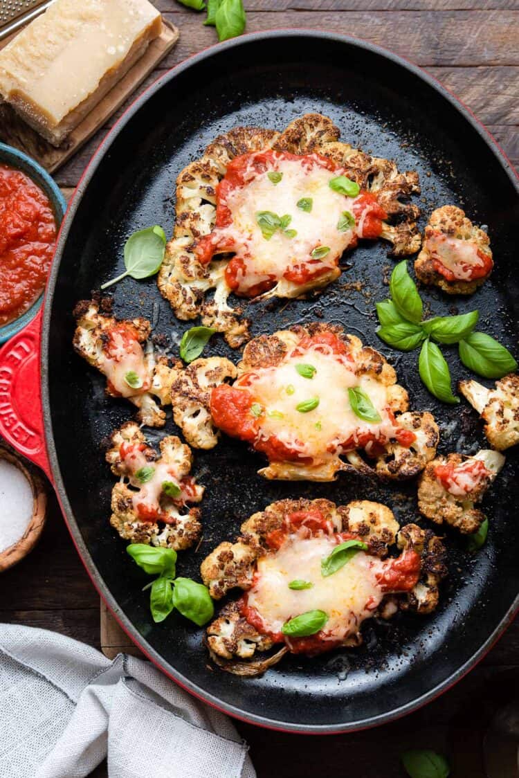 Baked Cauliflower Parmesan garnished with basil in a red Le Creuset pan.