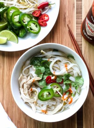 A bowl of easy thirty-minute pho made with poached chicken, fresh herbs, slices of lime, and a flavorful broth.