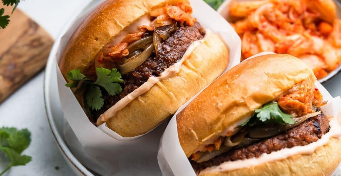 Kimchi Burgers wrapped in parchment in a bowl with a side of kimchi.