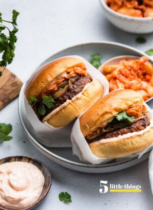 Kimchi Burgers wrapped in parchment in a bowl with a side of kimchi.