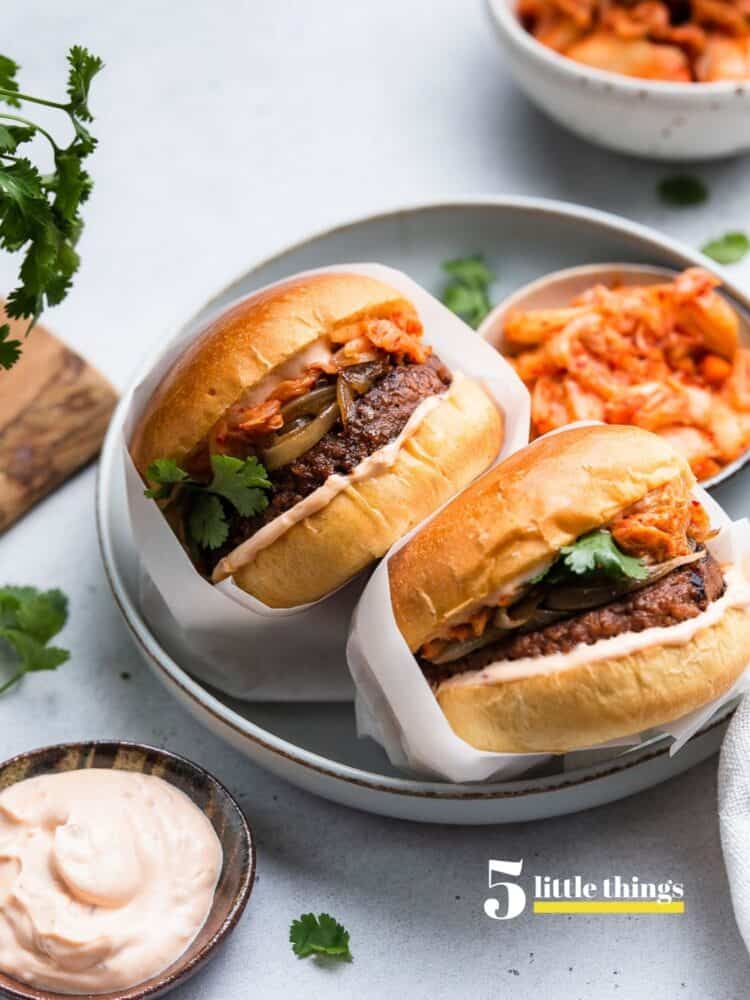 Kimchi Burgers wrapped in parchment in a bowl with a side of kimchi.