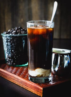 A glass of Homemade Thai Iced Coffee with coffee beans in the background.