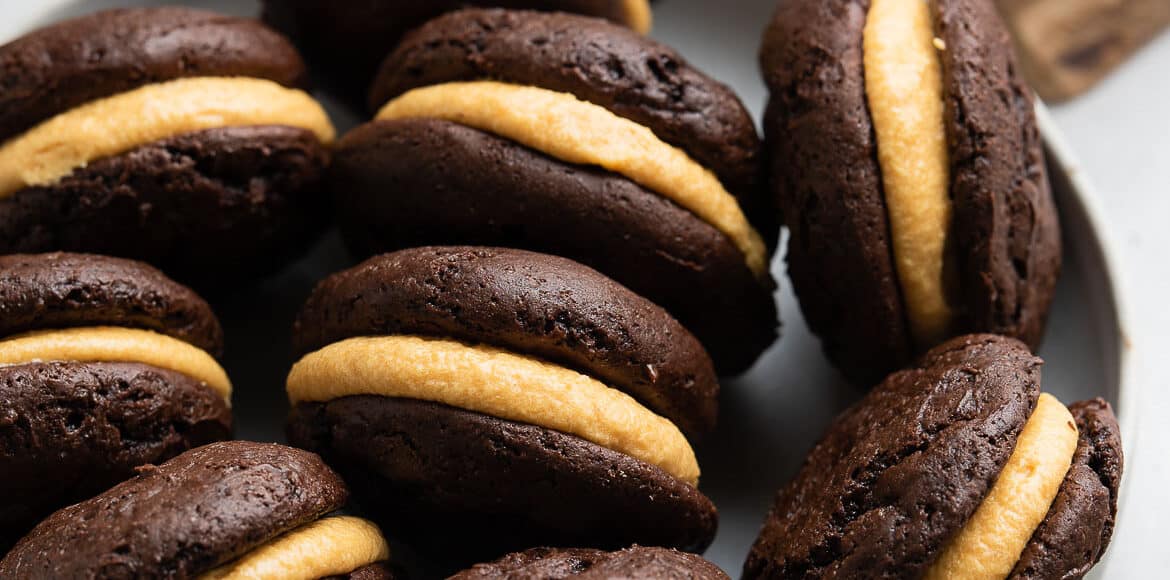 Chocolate Pumpkin Whoopie Pies in a light grey bowl with a cup of tea.