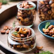 Spiced nuts in mason jars on a wooden tray.