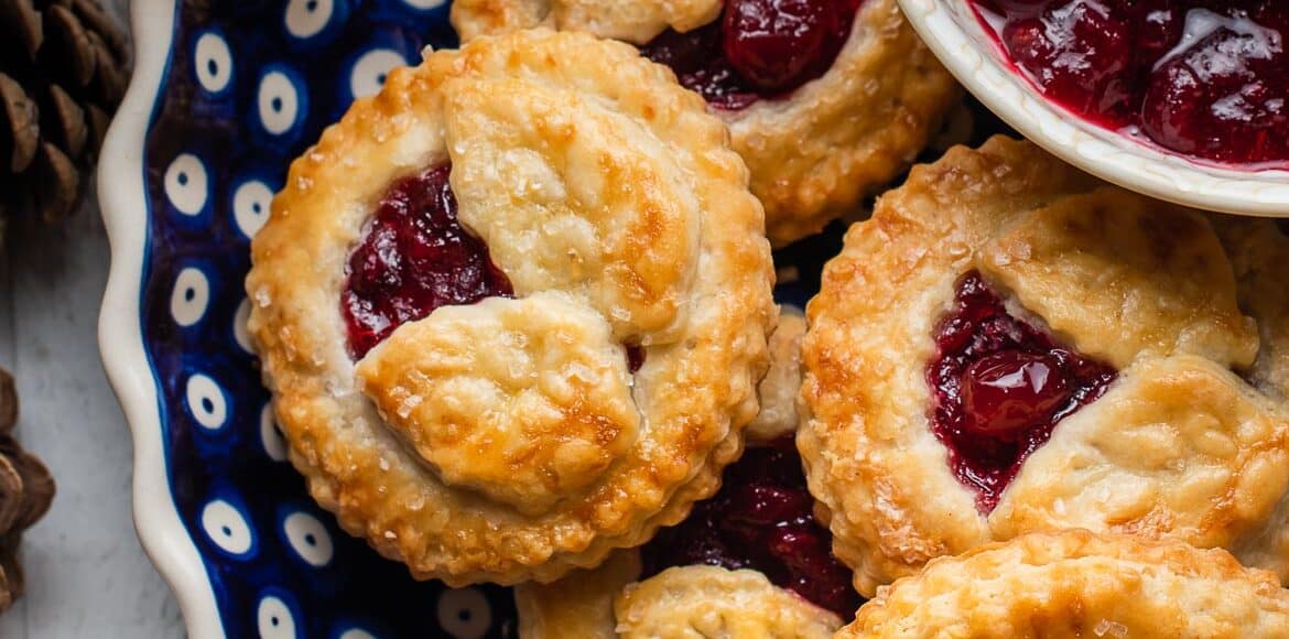 Cranberry Hand Pies in a blue ceramic pie dish with a bowl of cranberry sauce on the side.
