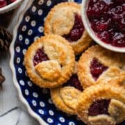 Cranberry Hand Pies in a blue ceramic pie dish with a bowl of cranberry sauce on the side.