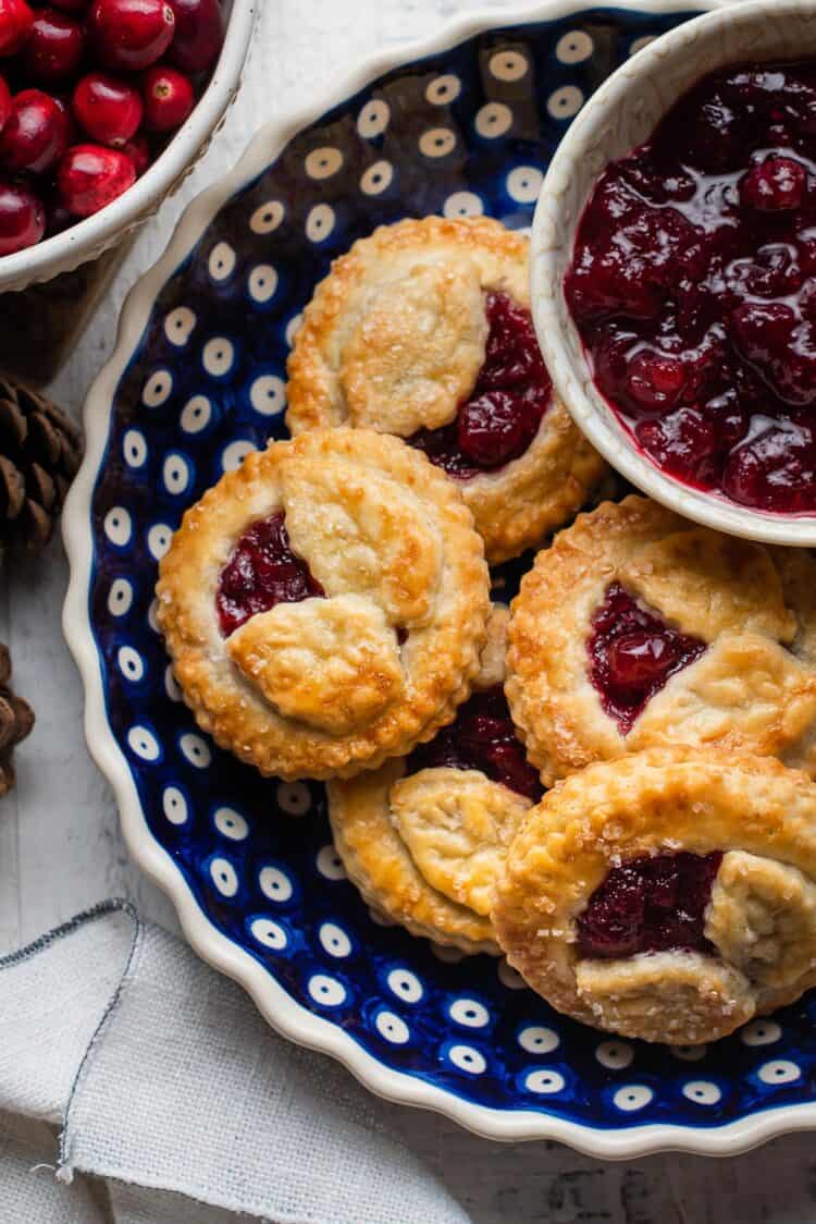 Cranberry Hand Pies in a blue ceramic pie dish with a bowl of cranberry sauce on the side.