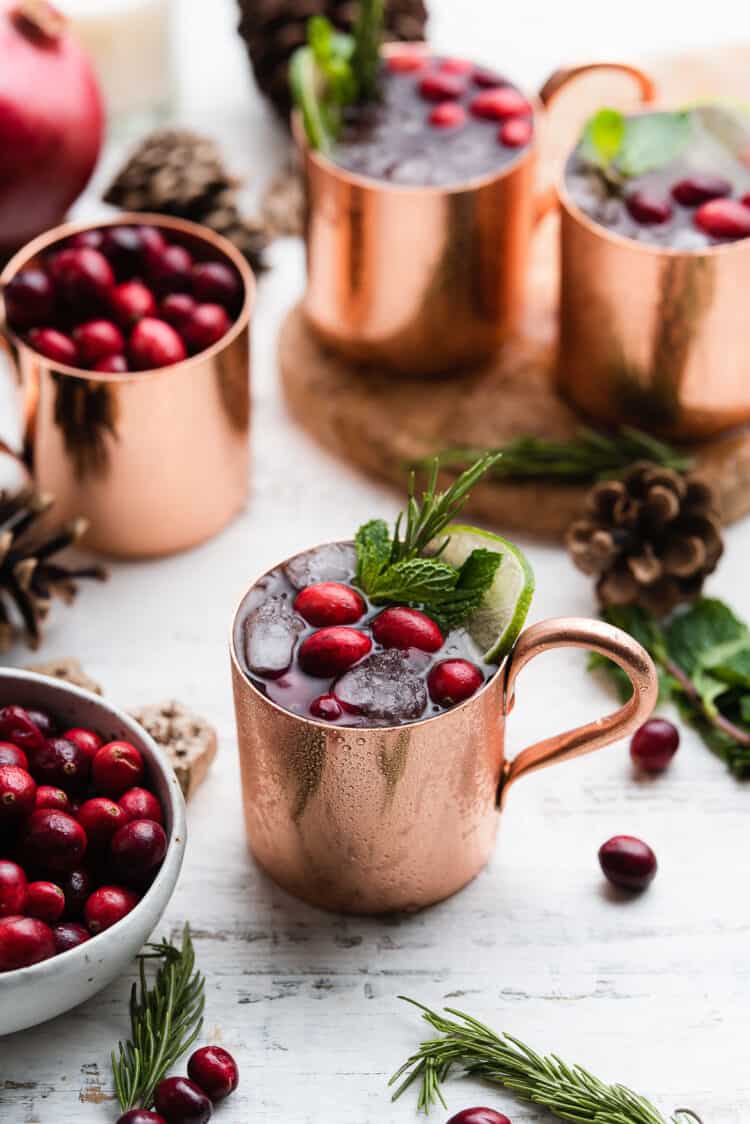 Cranberry Pomegranate Moscow Mule in a copper cup garnished with cranberries, mint, lime and rosemary.