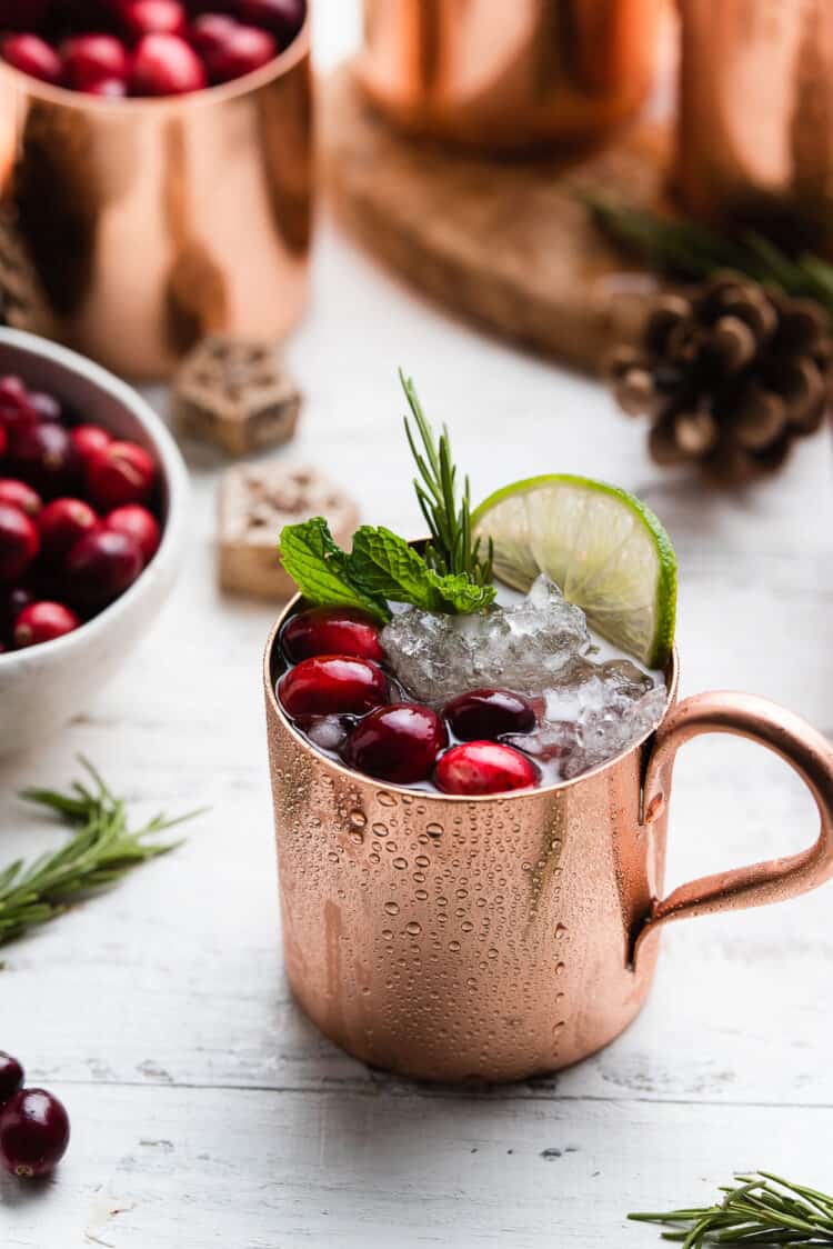 Pomegranate Cranberry Moscow Mule in a copper cup garnished with cranberries, mint, lime and rosemary.