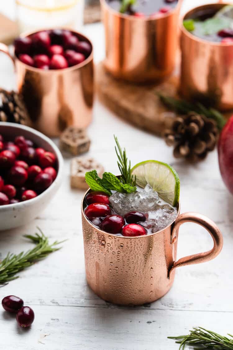 Pomegranate Cranberry Moscow Mule in a copper cup garnished with cranberries, mint, lime and rosemary.