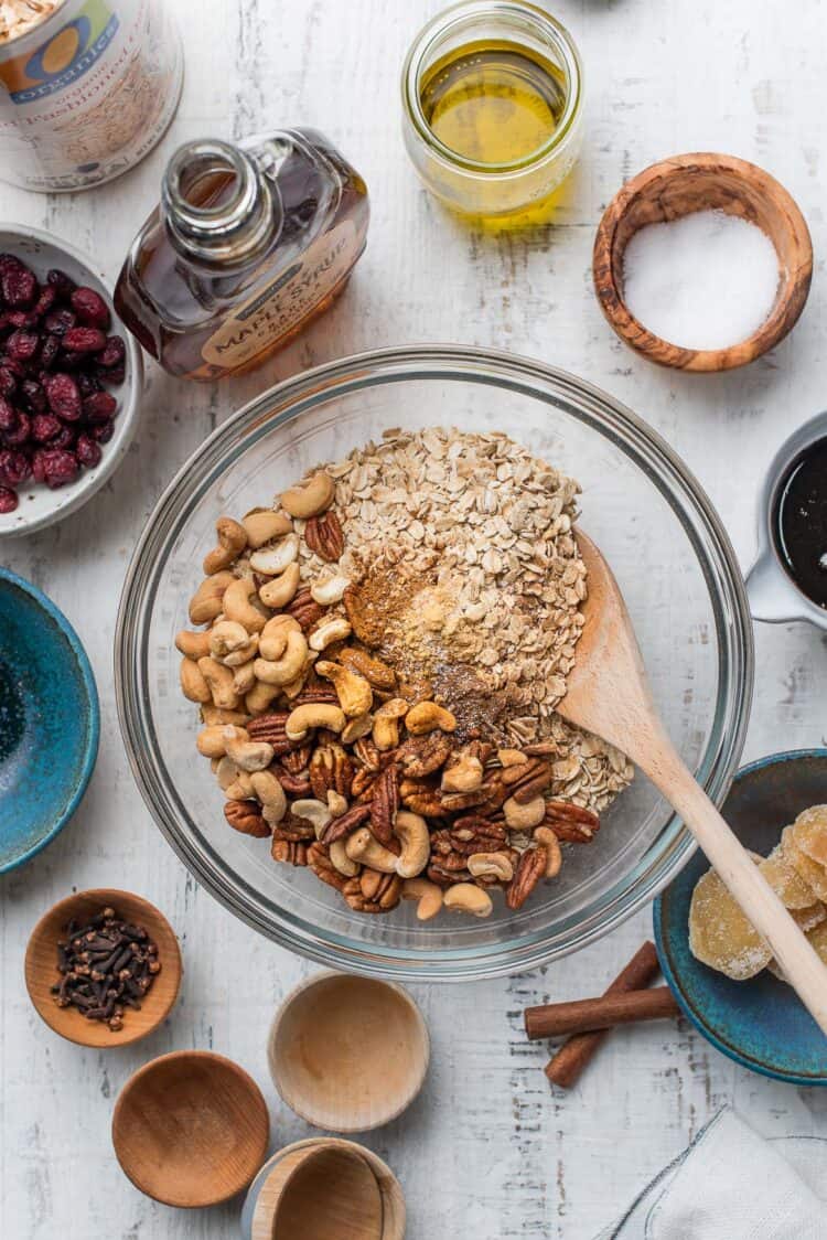 Ingredients for gingerbread granola in a clear mixing bowl.