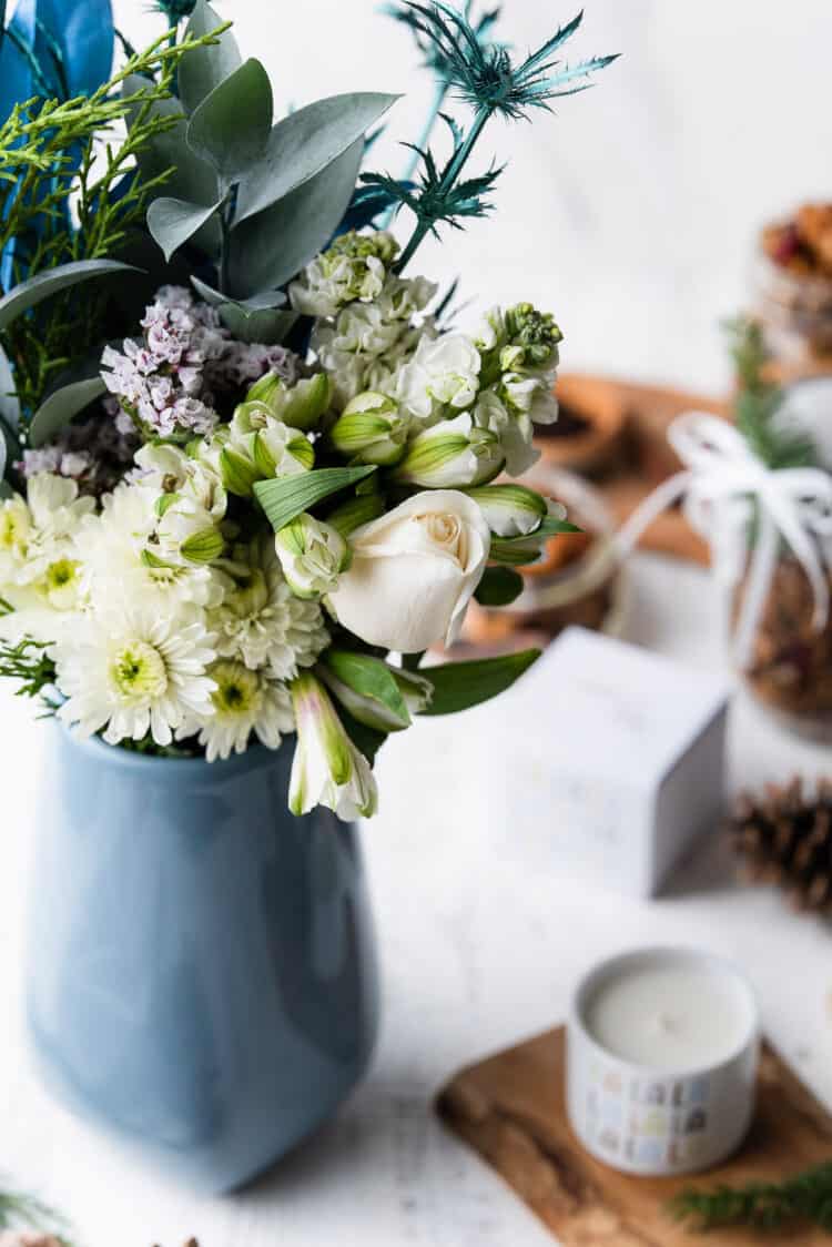 Debi Lilly white flowers in a blue vase next to a holiday candle.